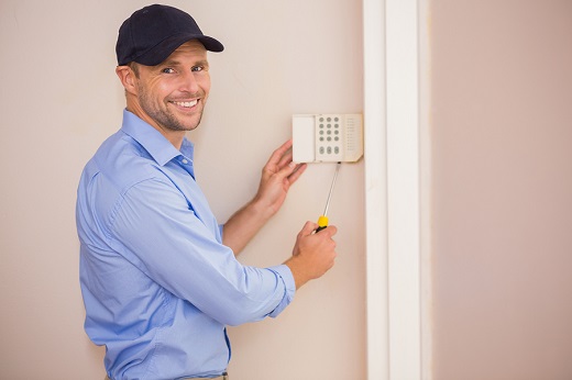Smiling handyman fixing an alarm system on the wall